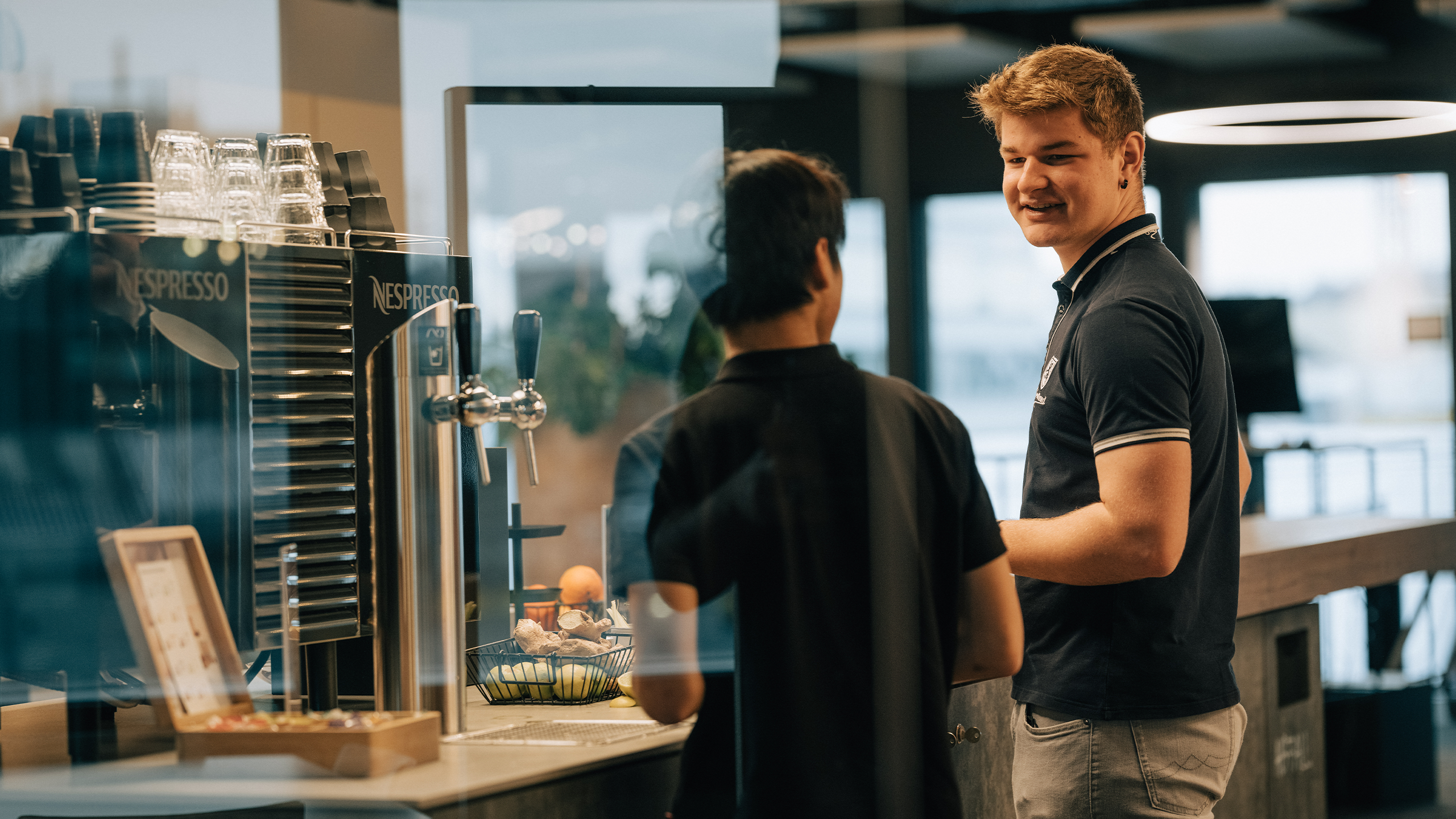 2 Lehrlinge unterhalten sich vor der Kaffeemaschine in einem Office
